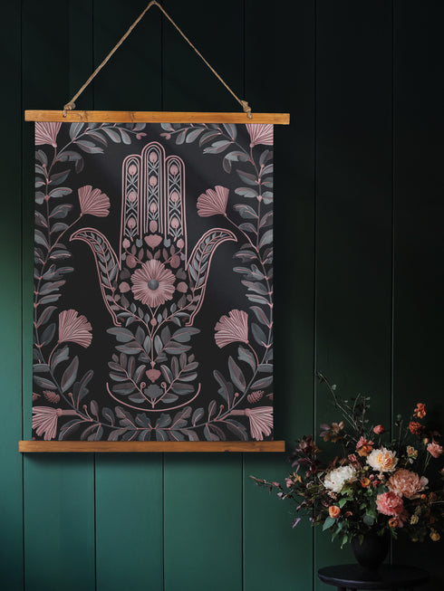 Botanical Hamsa wall tapestry featuring intricate rose gold and teal design on black background, showing a protective hand symbol surrounded by leaf motifs and floral elements, hanging from wooden dowels with natural twine.